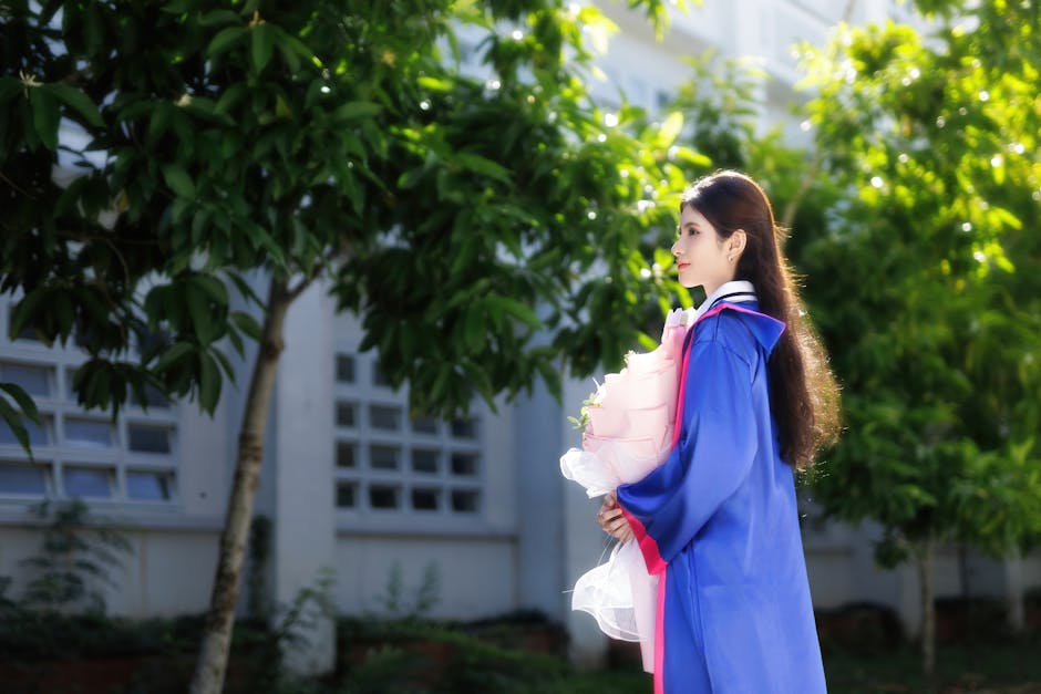 卒業式のガウンを着て、屋外で花束を持ち、自分の成果を祝っている若い女性。