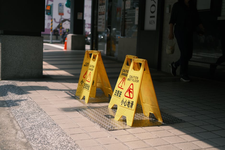 日当たりの良い屋外の歩道に、安全上の警告を示す黄色の「床が濡れています」という注意標識が設置されている。