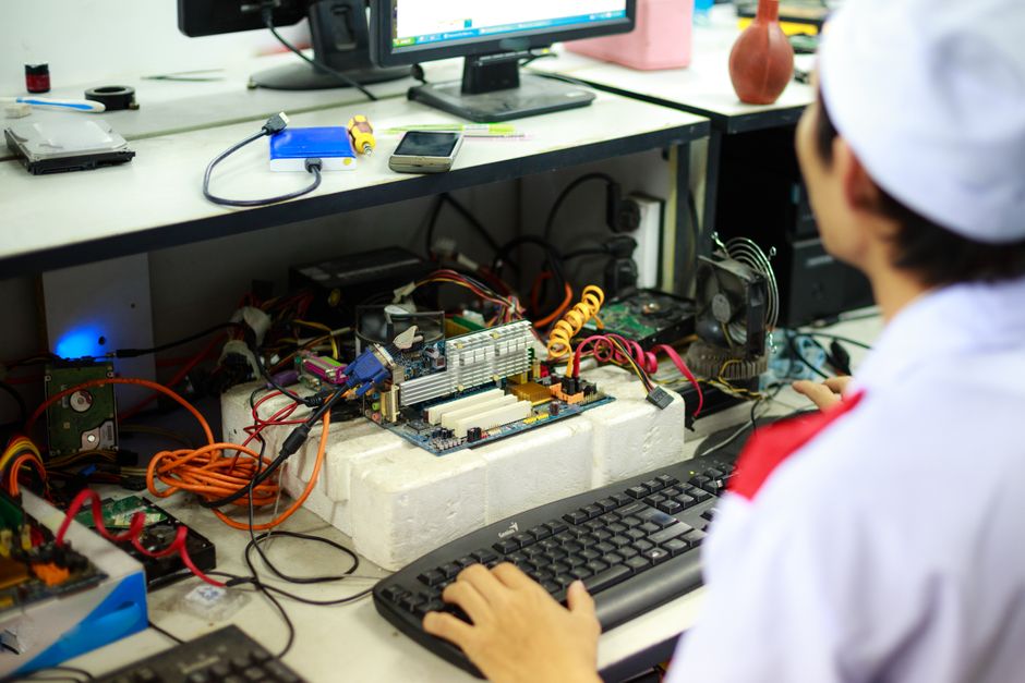 ラボユニフォームを着た男性が作業台でコンピュータ部品と配線に取り組んでいます。