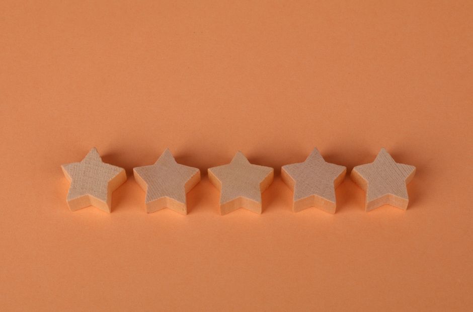 オレンジ色の表面に並べられた5つの星形の木製ブロックは、評価の概念を表現するのに最適です。