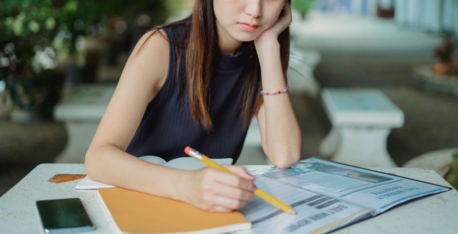 屋外で勉強している集中した若い女性、ノートに書き込む。