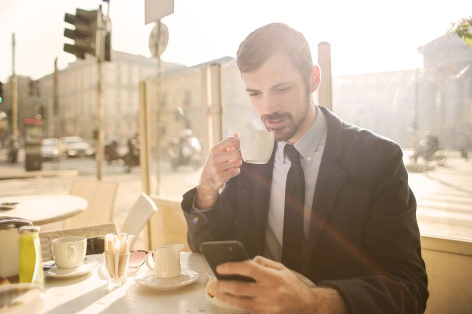 晴れた日にカフェでコーヒーを楽しみながらスマートフォンを使うビジネスマン。