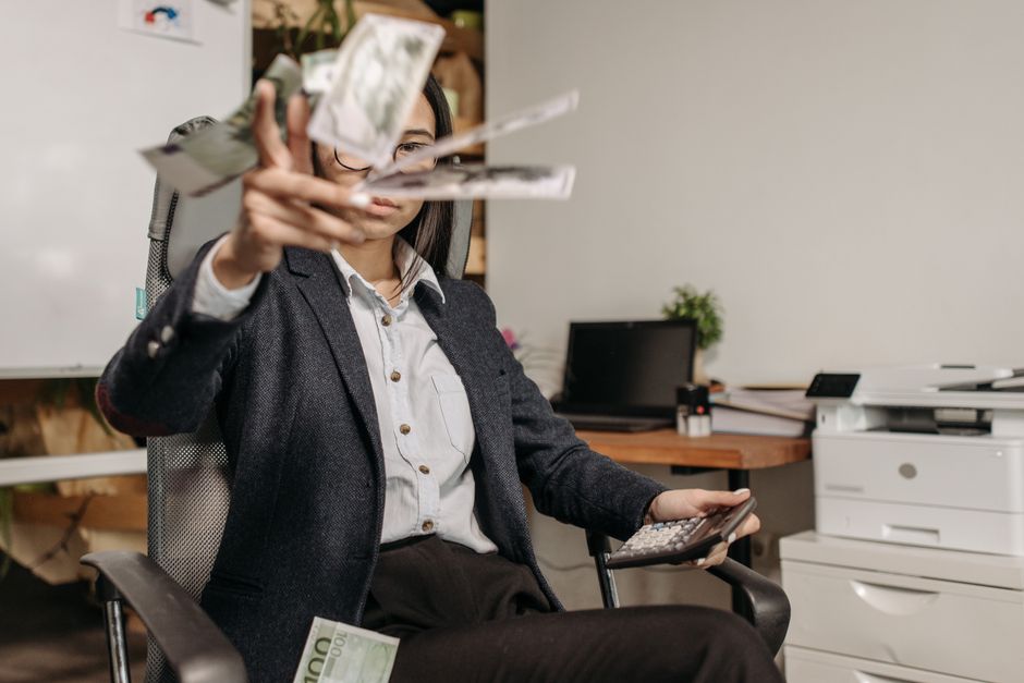 スーツを着たビジネスウーマンが、現代的なオフィスで財務を計算しながらお金を投げています。